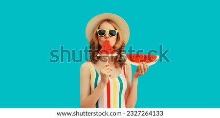 Summer portrait of happy young woman posing with fresh juicy fruits, lollipop or ice cream shaped slice of watermelon wearing straw hat, sunglasses on blue background