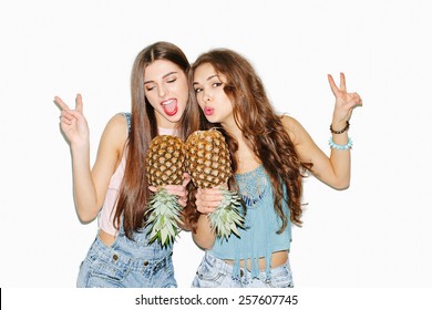 Summer Portrait Of Two Pretty Brunette Girl Friends Having Fun With Pineapple. Singing And Smiling. Casual Style, Bright Makeup, Pink Lips. White Background, Not Isolated. Inside