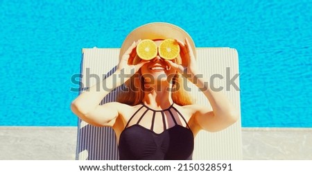 Summer portrait of woman covering her eyes with fresh slices of orange lying on deck chair on pool background