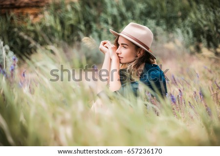 Summer portrait of young hipster woman sitting in a grass on sunny day.young slim beautiful woman,bohemian outfit,indie style, summer vacation,sunny,having fun, positive mood,romantic,woman in hat