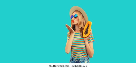 Summer portrait of young woman model posing with fresh papaya fruits wearing straw hat, sunglasses on blue background - Shutterstock ID 2313588675