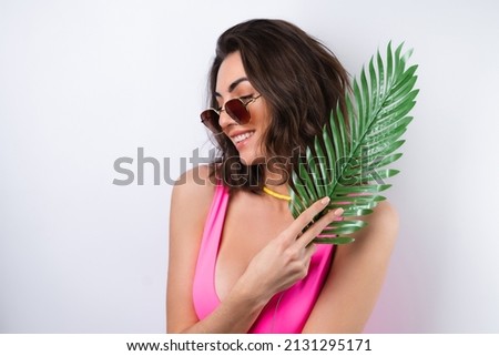 Summer portrait of young woman in pink swimsuit, bright yellow beach necklace with monstera palm leaf and sunglasses