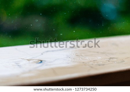 Summer rain raindrops falling down on wooden painted handle of balcony railings on blurred trees background