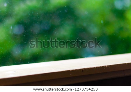 Summer rain raindrops falling down on wooden painted handle of balcony railings on blurred trees background