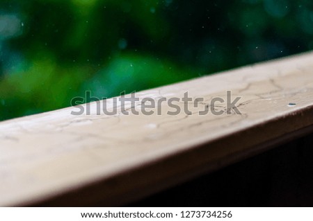 Summer rain raindrops falling down on wooden painted handle of balcony railings on blurred trees background