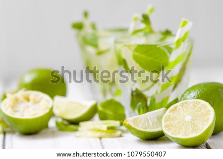 Summer refreshing cocktail mojito with lime and mint on white wooden vintage background. Fresh summertime iced drink with green citrus and fragrant leaves in beautiful glasses.
