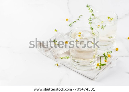 Summer refreshing drinks, infused herbal water, iced tea. Chamomile Honey and Whiskey Cocktail with thyme in glasses, on a white marble table. Copy space