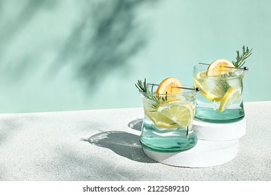 Summer refreshing lemonade drink or alcoholic cocktail with ice, rosemary and lemon slices on pastel light green surface. Fresh healthy cold lemon beverage. Water with lemon. - Shutterstock ID 2122589210