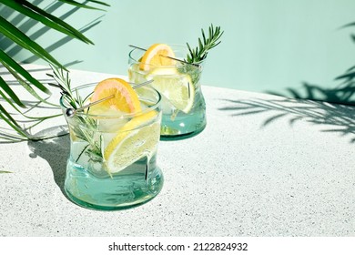 Summer refreshing lemonade drink or alcoholic cocktail with ice, rosemary and lemon slices on pastel light green surface. Fresh healthy cold lemon beverage. Water with lemon. - Shutterstock ID 2122824932