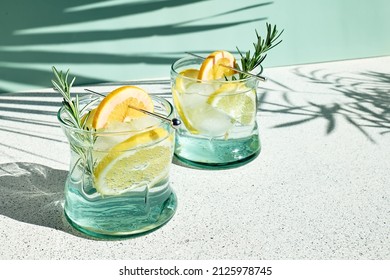 Summer refreshing lemonade drink or alcoholic cocktail with ice, rosemary and lemon slices on pastel light green surface. Fresh healthy cold lemon beverage. Water with lemon. - Powered by Shutterstock