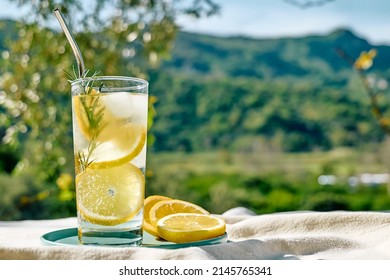 Summer refreshing lemonade drink or alcoholic cocktail with ice, rosemary and lemon slices on the table in the garden. Fresh healthy cold lemon beverage. Water with lemon. - Powered by Shutterstock