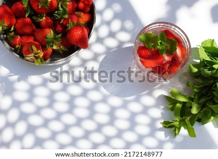 Summer refreshing strawberry and mint drink, mint bunch and strawberies in a bowl top view with  sunlight abstract shadow on desk. Copy space