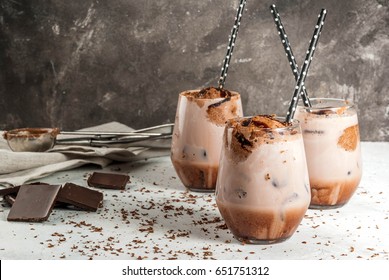 Summer refreshment drinks. Chilled iced chocolate cocoa. With scoop of chocolate ice cream, chocolate powder and ice. In glasses, with tubes for drinking. White concrete table. Copy space
