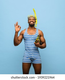 Summer Rest. Funny Africam-American Man In Swimming Suit, Goggles Holding Swim Fins Isolated On Blue Background. Retro Style. Concept Of Facial Expression, Holidays, Funny Meme Emotions.