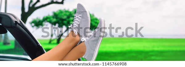 Summer road trip car fun woman sleeping with feet\
out the window of convertible sports car on travel vacation getaway\
banner panoramic background. Girl relaxing, closeup of legs and\
shoes.