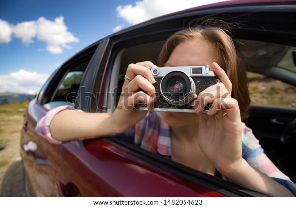 Summer Road Trip. Girl with retro camera\
taking pictures from the car window.\
\
