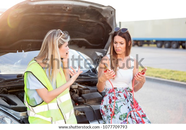 Summer road trip gone wrong. Two young\
women stranded by the broken car, calling for\
help.