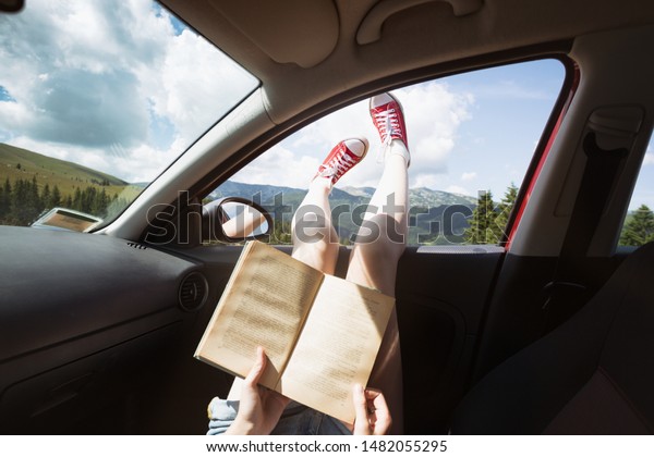 Summer Road Trip. Happy\
beautiful girl traveling in a car.  reads a book across  at the\
mountains\
