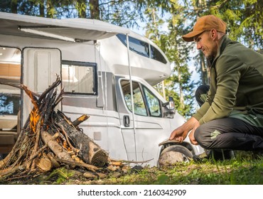 Summer Road Trip And Van Life Theme. Caucasian Men Hanging Out Near Campfire And Camping In A Camper Van RV Recreational Vehicle.