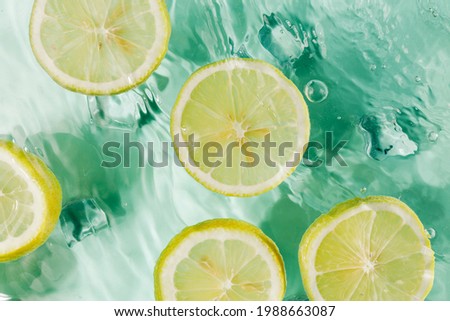 Summer scene with round slices of lemons floating in the turquoise water. Creative food or drink concept. Refreshing drink with ice cubes and fruit in splash of water. Flat lay, top view. 