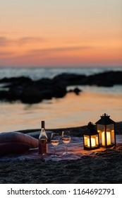 Summer sea sunset. Romantic picnic on the beach. Bottle of wine, glasses, candles, plaid and pillows. Selective focus.