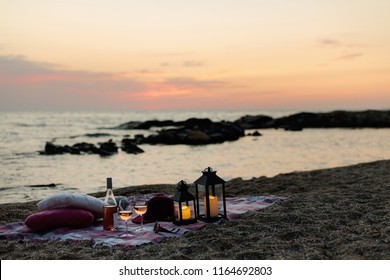 Summer sea sunset. Romantic picnic on the beach. Bottle of wine, glasses, candles, plaid and pillows. Selective focus. - Powered by Shutterstock