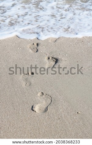 Summer sea wave with sea foam washes away footprints in sand