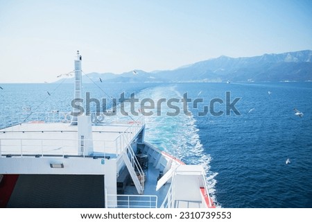 Summer seascape with seagulls flying around ferry. Sea water waves trails from ferry boat. View from the ferries. Sunny clear blue sky. Mountain landscape of Thassos, Greece.	