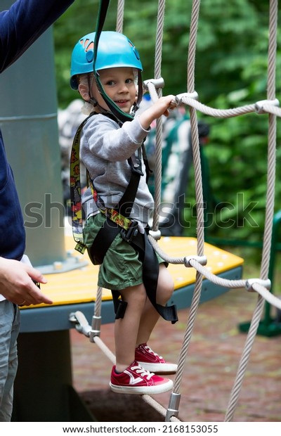 Summer. A small child\
climbs in a rope park on a rope bridge. A boy is having fun in an\
Adventure Park. A male baby on a climbing frame. Compliance with\
safety techniques.