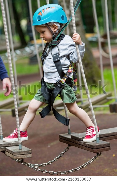 Summer. A small child
climbs in a rope park on a rope bridge. A boy is having fun in an
Adventure Park. A male baby on a climbing frame. Compliance with
safety techniques.