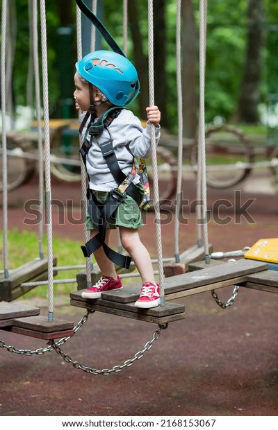 Summer. A small child\
climbs in a rope park on a rope bridge. A boy is having fun in an\
Adventure Park. A male baby on a climbing frame. Compliance with\
safety techniques.