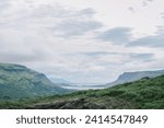 Summer in Southern Iceland nature landscape background with calm serene water, green rocky scenic mountains, and textured moody cloudy sky