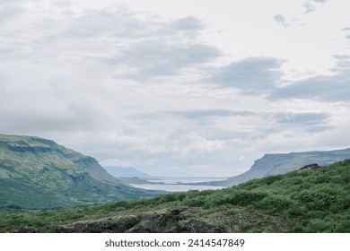 Summer in Southern Iceland nature landscape background with calm serene water, green rocky scenic mountains, and textured moody cloudy sky - Powered by Shutterstock