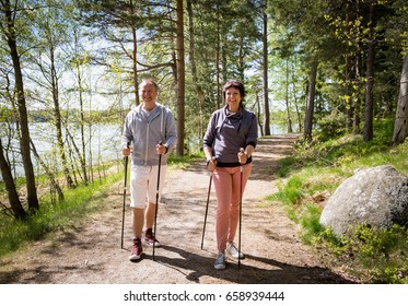 Summer Sport In Finland - Nordic Walking. Man And Mature Woman Hiking In Green Sunny Forest. Active People Outdoors. Scenic Peaceful Finnish Summer Landscape.