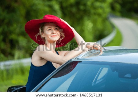 Summer sports girl in a big red hat and mini dress, next to the car, nature, field.