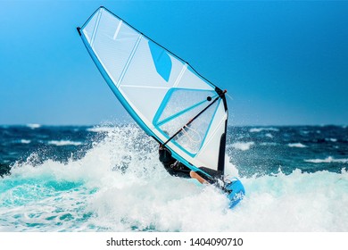 summer sports: windsurfer riding the waves during the holidays with the white sail on the atlantic blue ocean water.
