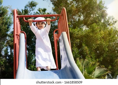 Summer Spring Break Of Arab Student Boy. Emirati Kid On Vacation Playing Slide At A Park Spending Time With Family. Young Boy On White Clothing Kandura In Dubai UAE Middle East Countries