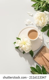 Summer or spring breakfast with coffee, white peonies flowers, craft envelope on gray background with sunny shadow. Spring vertical workplace, top view, flat lay.