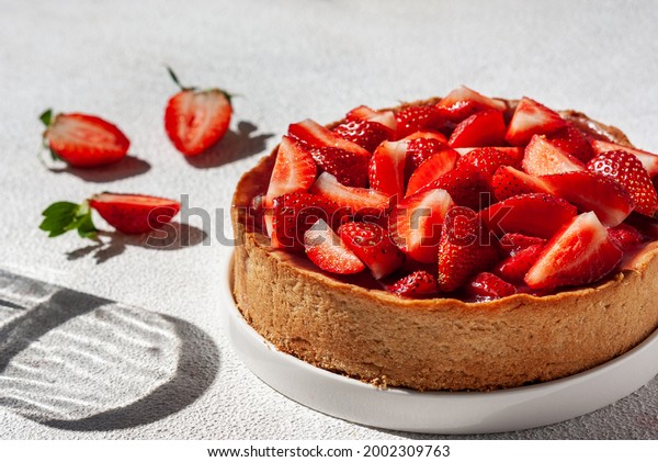 Summer strawberry pie on white table with hard\
shadows of glass goblet,\
close-up