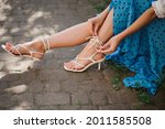Summer street fashion details: close up of  trendy white leather strappy  sandals  with classic heels.  Woman wearing elegant outfit, posing outdoor. Copy, empty  space for text