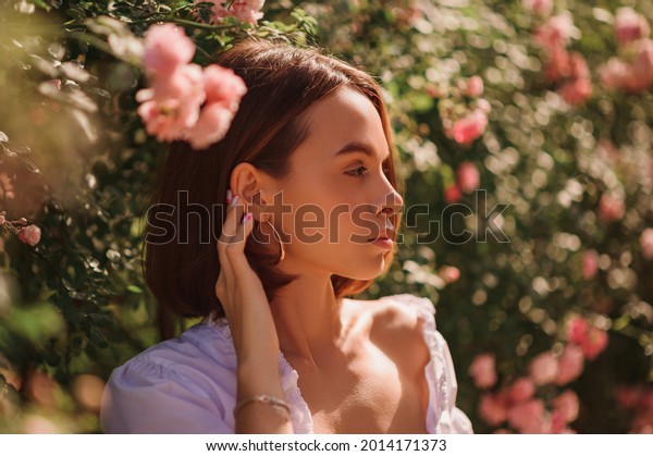 Summer\
street style, fashion portrait of beautiful brunette woman with\
elegant bob hairstyle,  wearing white blouse, posing in street,\
near blooming roses. Copy, empty space for\
text\
