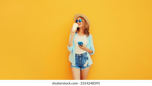 Summer stylish happy young woman drinking coffee with phone, cool girl using smartphone holding cup of coffee dressed tourist straw hat looking away standing on yellow background - Powered by Shutterstock