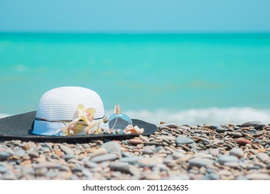 Summer stylish sun hat with a Bottle of women's perfume a sprig of orchid flowers and seashells on sea stones in the sunlig.Women's summer accessories aganst background of azure color water sea
