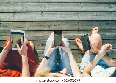 Summer Sunny Day. Top View, Computer Tablet And Smart Phones In The Hands Of The Three Girls Sitting Outside On A Wooden Platform. Young Women Using Digital Gadgets