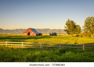 Summer sunset with a red barn and silos in rural Montana with Rocky Mountains in the background.
