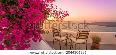 Summer sunset vacation scenic of luxury famous Europe destination. White architecture in Santorini, Greece. Stunning travel scenery with pink flowers chairs, terrace sunny blue sky. Romantic street