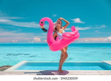 Summer suntan woman wearing hat and sunglasses for sun protection while sunbathing on Caribbean beach vacation by luxury infinity swimming pool. Fun flamingo pool toy air float.