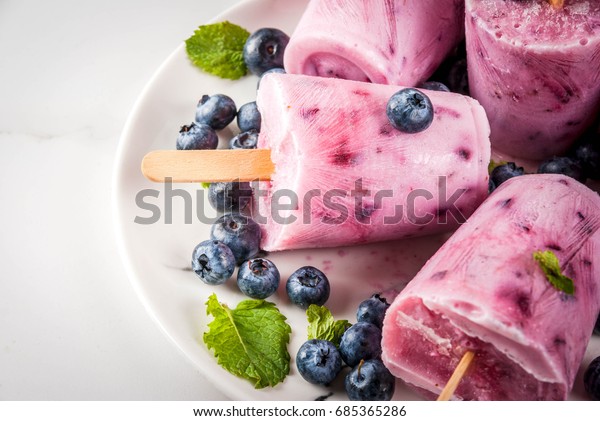 Summer sweets and desserts. Vegan food. Frozen\
drinks, smoothies. Ice cream popsicles from homemade Greek yogurt\
and fresh organic blueberries. With mint. On plate, white table.\
Copy space