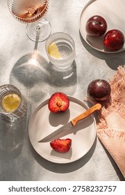 Summer table set with fruit. Two plates of plums, water with lemon, wine.  Sunny day. Top view.