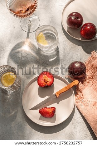 Summer table set with fruit. Two plates of plums, water with lemon, wine.  Sunny day. Top view.